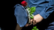 Ein Polizist hält bei einem Gedenken am Ende eines Schweigemarschs der "Blaulichtfamilie" von der Deutschen Polizeigewerkschaft (DPolG) und der Gewerkschaft der Polizei (GdP) für den durch einen Messerangriff in Mannheim zu Tode gekommenen Polizisten eine Rose. © dpa Foto: Christoph Soeder