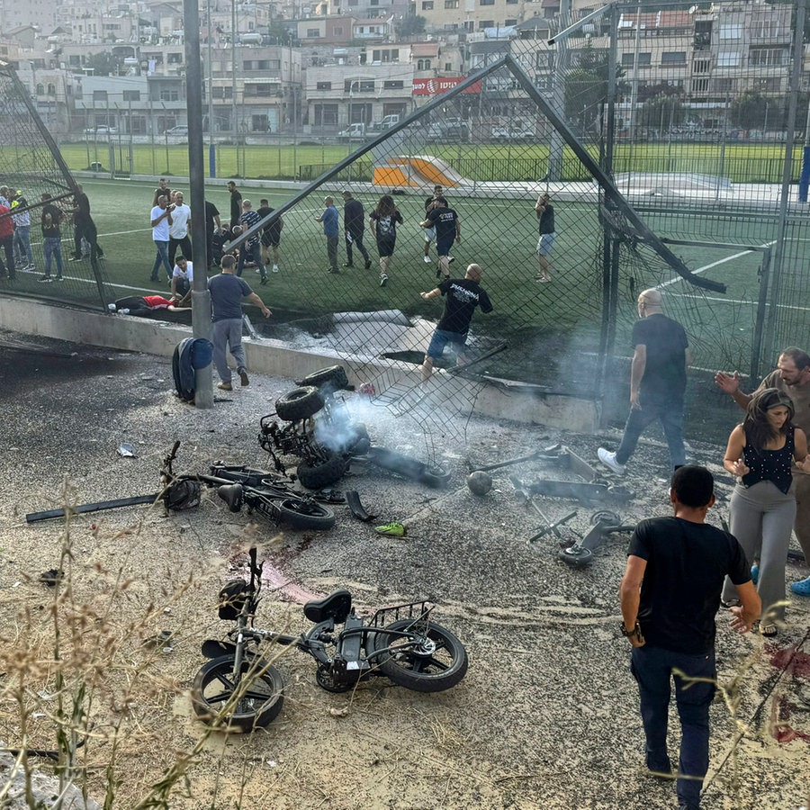 Anwohner eilen verletzten Kindern zu Hilfe, kurz nachdem eine Rakete ein Fußballfeld auf den israelisch kontrollierten Golanhöhen getroffen hat. © AP/dpa Foto: Hassan Shams