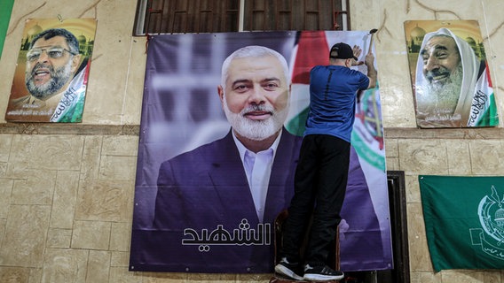 Ein Palästinenser hängt ein großes Bild von Ismail Hanija in einer Halle im palästinensischen Flüchtlingslager Burj al-Brajneh auf. © dpa Foto: Marwan Naamani