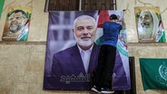 Ein Palästinenser hängt ein großes Bild von Ismail Hanija in einer Halle im palästinensischen Flüchtlingslager Burj al-Brajneh auf. © dpa Foto: Marwan Naamani