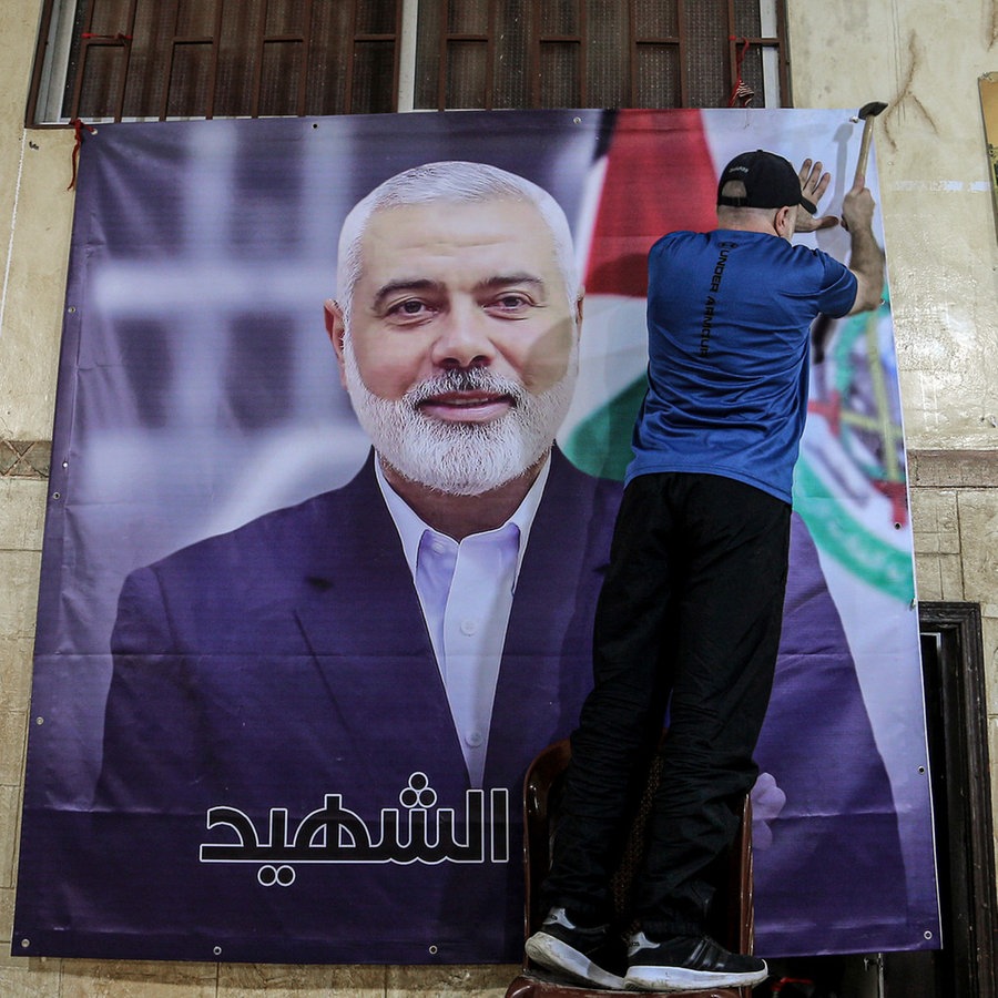 Ein Palästinenser hängt ein großes Bild von Ismail Hanija in einer Halle im palästinensischen Flüchtlingslager Burj al-Brajneh auf. © dpa Foto: Marwan Naamani