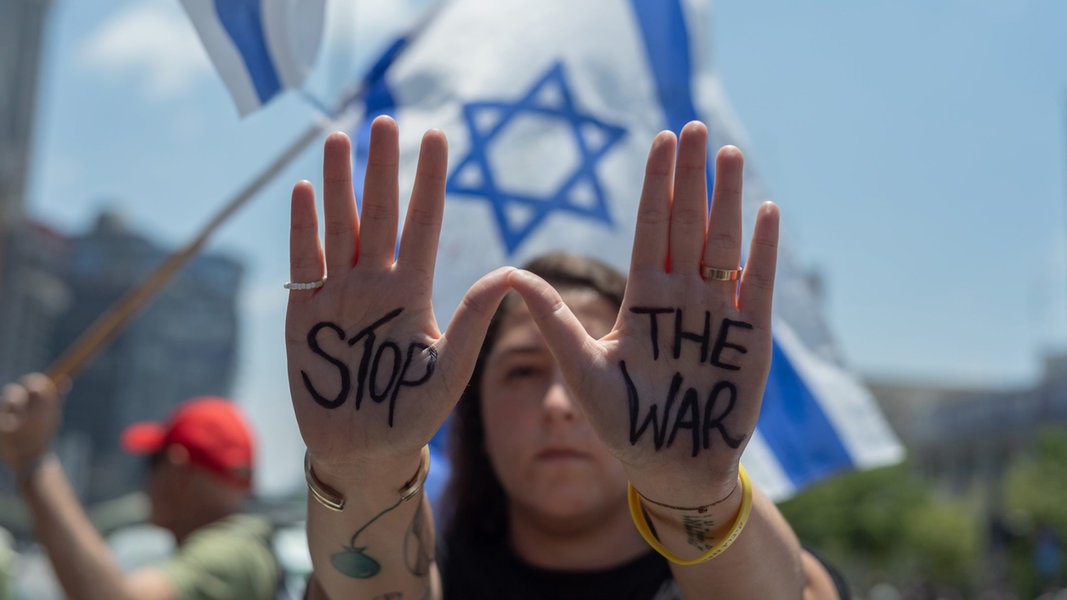 Eine israelische Demonstrantin hält ihre Hände mit der Aufschrift "Stop the War" hoch vor einer israelischen Flagge im Hintergrund, während einer Kundgebung in Tel Aviv. © dpa Foto: Ilia Yefimovich