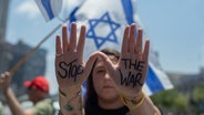Eine israelische Demonstrantin hält ihre Hände mit der Aufschrift "Stop the War" hoch vor einer israelischen Flagge im Hintergrund, während einer Kundgebung in Tel Aviv. © dpa Foto: Ilia Yefimovich