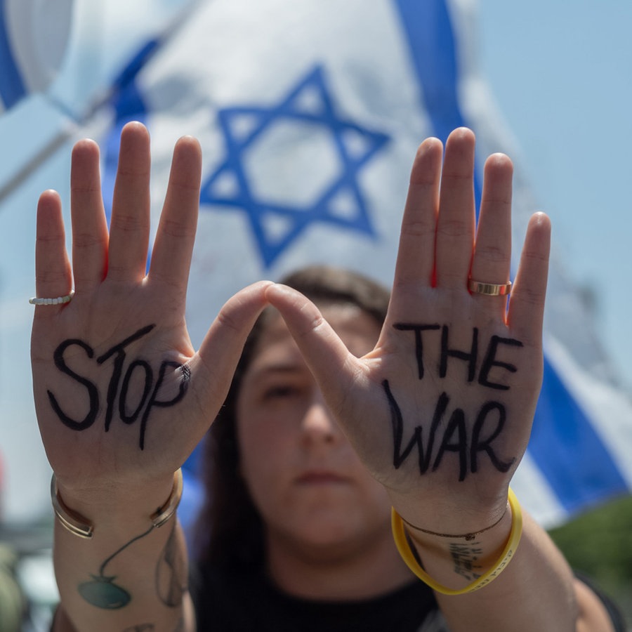 Eine israelische Demonstrantin hält ihre Hände mit der Aufschrift "Stop the War" hoch vor einer israelischen Flagge im Hintergrund, während einer Kundgebung in Tel Aviv. © dpa Foto: Ilia Yefimovich