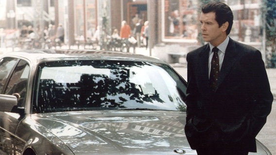 Das Archivbild von 1997 zeigt Pierce Brosnan vor seinem "Dienstwagen", einem BMW 750 iL, in einer Szene des James-Bond-Films "Der Morgen stirbt nie". © picture-alliance / dpa | dpa-Film_BMW 