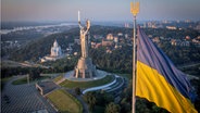 Die ukrainische Nationalflagge weht, während Arbeiter das ukrainische Wappen auf das Schild in der Hand des Mutterland-Denkmals montieren, nachdem ein Staatswappen der Sowjetunion vom Schild entfernt worden ist. © AP/dpa Foto: Efrem Lukatsky