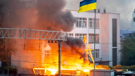 Die ukrainische Flagge ist vor dem Rauch eines Feuers zu sehen, nach russischen Angriffen auf Kiew. © ZUMA Press Wire/dpa Foto: Andreas Stroh