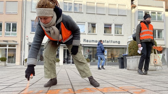 Eine Klimaaktivistin besprüht den Gehweg mit orangener Farbe. © ARD/SWR Foto: Sophie Rebmann