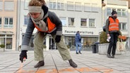 Eine Klimaaktivistin besprüht den Gehweg mit orangener Farbe. © ARD/SWR Foto: Sophie Rebmann