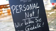 Auf einer Tafel am Eingang zu einem Biergarten ist der Schriftzug "Personalnot! Wir bitten Sie um Geduld!" zu lesen. © picture alliance Foto: Matthias Balk