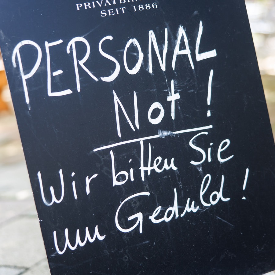 Auf einer Tafel am Eingang zu einem Biergarten ist der Schriftzug "Personalnot! Wir bitten Sie um Geduld!" zu lesen. © picture alliance Foto: Matthias Balk