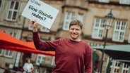 Podcaster Mario Neumann steht mit einem Schild "eine Stunde reden" in Bremen. © Radio Bremen Zwei 