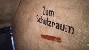 "Zum Schutzraum" steht an einer Wand im Keller eines Hauses. © greatif Foto: Marita Gaul