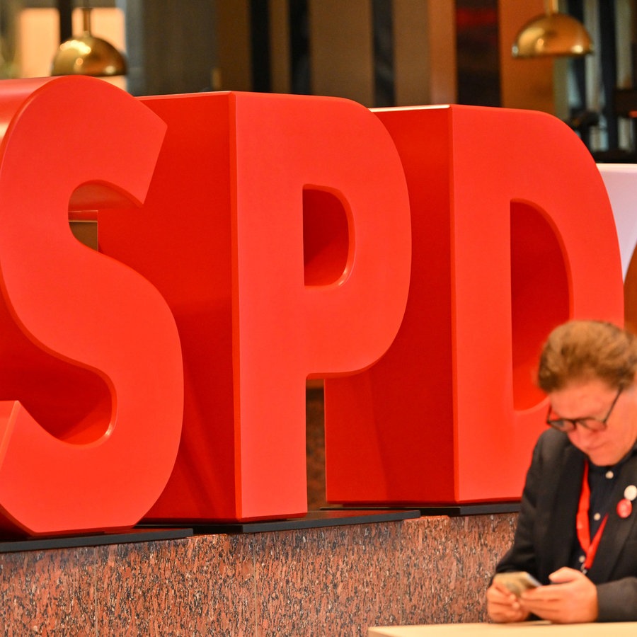 Ein SPD-Mitglied steht beim Landesparteitag der SPD Baden-Württemberg vor einem Partei-Logo. © dpa Foto: Jan-Philipp Strobel