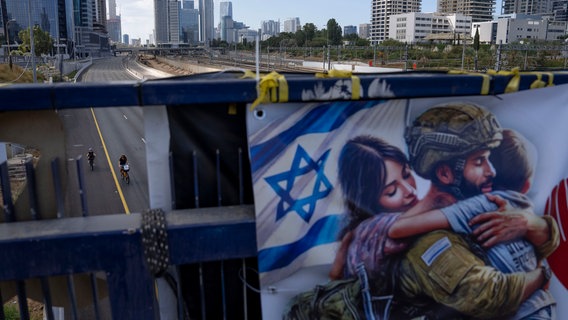 Auf einer Brücke hängt während des jüdischen Feiertags Jom Kippur in Tel Aviv (Israel) ein Plakat mit mit der israelischen Fahne neben einem Sodaten und seiner Frau, der sein Kind gerade umarmt. © AP/dpa Foto: Oded Balilty