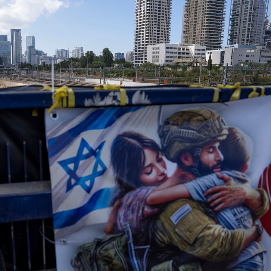 Auf einer Brücke hängt während des jüdischen Feiertags Jom Kippur in Tel Aviv (Israel) ein Plakat mit mit der israelischen Fahne neben einem Sodaten und seiner Frau, der sein Kind gerade umarmt. © AP/dpa Foto: Oded Balilty