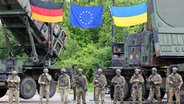 Deutsche und ukrainische Soldaten stehen beim Besuch des ukrainischen Präsidenten Selenskyj auf einem Truppenübungsplatz vor Flugabwehrraketensystemen vom Typ Patriot. © dpa Foto: Jens Büttner