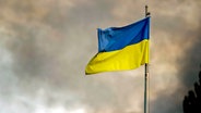 Die ukrainische Flagge ist vor dem Rauch eines Feuers zu sehen, nach russischen Angriffen auf Kiew. © ZUMA Press Wire/dpa Foto: Andreas Stroh