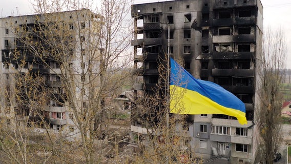 Eine ukrainische Fahne weht vor von russischen Raketen zerstörten Gebäuden in Kiew. © IMAGO / Lehtikuva Foto: Lehtikuva