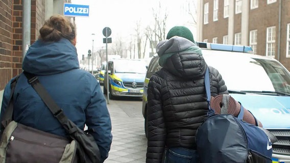 Zwei Frauen, von hinten zu sehen, gehen auf einer Straße in Richtung einer Polizeiwache. © NDR Foto: Sebastian Heidelberger