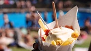 Ein Badegast in einem Freibad hält eine Portion Pommes Frites mit Ketchup und Mayonnaise in der Hand © picture alliance/dpa Foto: Julian Weber