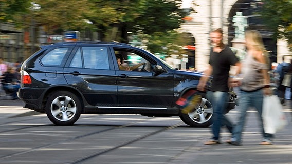 Ein BMW X5-Geländewagen fährt auf einer Straße an Fußgängern vorbei. © dpa picture alliance Foto: Gaetan Bally