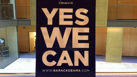 Ein Schild mit der Aufschrift "Yes we can" steht auf einem Tisch. © NDR Foto: Anna Engelke