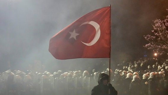 Ein Mann hält vor einem riesigen Polizeiaufgebot eine türkische Flagge während einer Demonstration gegen die Verhaftung des Istanbuler Bürgermeisters Imamoglu © AP/dpa Foto: Khalil Hamra