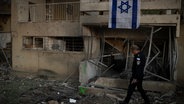 Ein israelischer Polizist läuft an einem durch eine Rakete zerstörten Gebäude in der nordisraelischen Stadt Karmiel vorbei. © picture alliance / ASSOCIATED PRESS | Leo Correa 