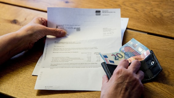 Eine Person schaut sich ein Schreiben der Deutschen Rentenversicherung an und hält dabei eine Geldbörse mit wenig Bargeld in den Händen. © picture alliance / Fotostand Foto: Fotostand / K. Schmitt