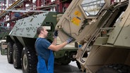 Ein Mitarbeiter von Rheinmetall arbeitet an einem Panzer vom Typ Fuchs in der Fertigungshalle von Rheinmetall © picture alliance/dpa Foto: Swen Pförtner