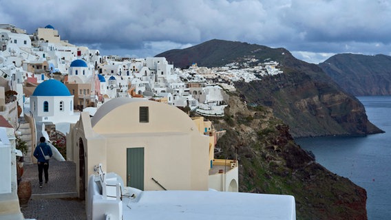 Ein Tourist nähert sich einer orthodoxen Kirche mit blauer Kuppel in Oia auf der erdbebengeschädigten Insel Santorini. © Petros Giannakouris/AP/dpa 