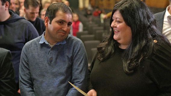 Bilal Rashid und Carolina Vásquez Álvarez sprechen bei einer Einbürgerungsfeier im Hamburger Rathaus miteinander. © Screenshot 