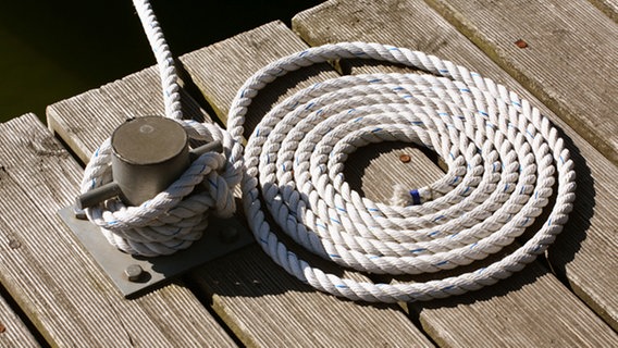 Das Seil, mit dem ein Boot am der Klampe festgebunden ist, liegt kreisförmig aufgerollt daneben auf einem Anlegesteg. © picture-alliance/ dpa Foto: Wolfram Steinberg
