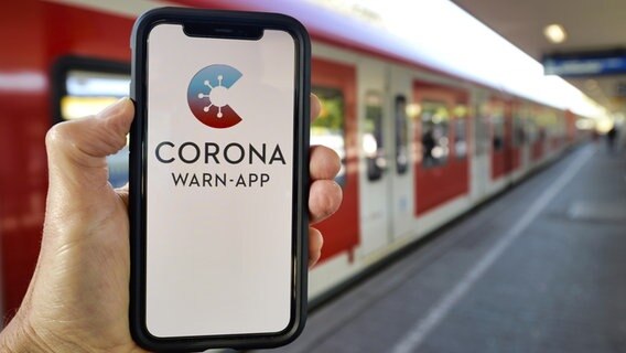 Ein Handy mit der Corona Warn-App wird vor einem Zug in die Luft gehalten. © dpa picture alliance Foto: Michael Weber