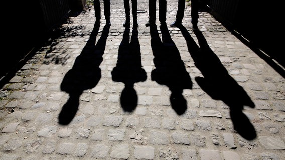 Vier Personen stehen auf einer gepflasterten Straße im Gegenlicht. © Mr. Nico / photocase.de Foto: Mr. Nico