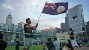 Ein Demonstrant in Hongkong mit Mundschutz schwenkt die britische Kolonialflagge in einem Park. © dpa picture alliance Foto: Vincent Yu