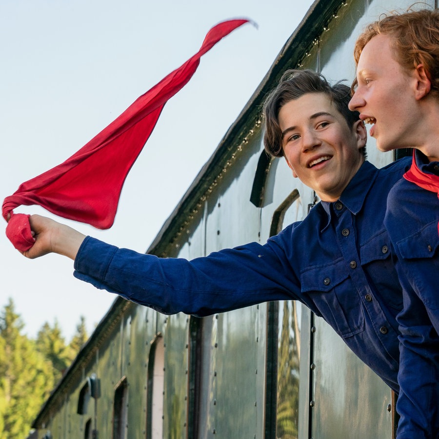 Zwei Jugendliche gucken aus dem Zug und schwenken eine Fahne. © LOOKSfilm 