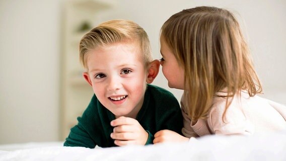 Zwei Kinder flüstern sich im Bett liegend etwas zu. © Bildagentur-online/Tetra Images 