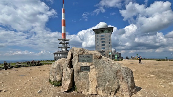 Eine weißrote Antenne, davor ein Felsen, auf dem eine Plakette mit der Inschrift "Brocken" steht, dahinter ein hohes Gebäude © NDR Foto: Carsten Vick