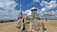 Eine weißrote Antenne, davor ein Felsen, auf dem eine Plakette mit der Inschrift "Brocken" steht, dahinter ein hohes Gebäude © NDR Foto: Carsten Vick