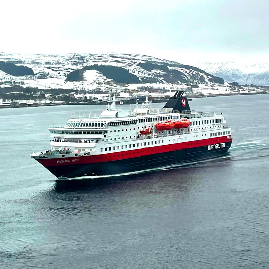 Ein weiß rotes Schiff fährt durch einen Fjord in der Landschaft der Hurtigruten in Norwegen, dahinter eine Landschaft mit Schnee © NDR Foto: Wiebke Keuneke / Mark Diening