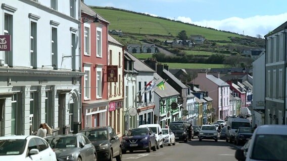 Eine Häuserzeile mit bunten Fassaden, leicht bergabführend, davor parken PKW - in Dingle, Irland © NDR Foto: Matthias Schuch