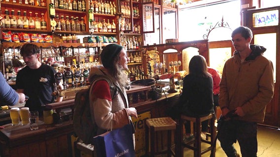 Junge Menschen in einem Pub mit Regalen voller Flaschen, Zapfhähnen und einem Holztresen in Irland © NDR Foto: Matthias Schuch