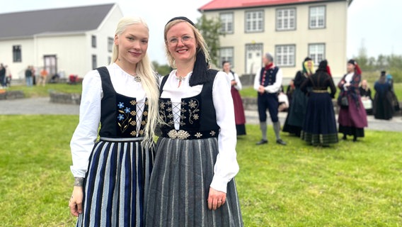 Zwei lächelnde Frauen stehen im Vordergrund in isländischen Trachten, dahinter sind weitere Menschen und zwei Gebäude unscharf zu erkennen © NDR Foto: Max-Marian Unger