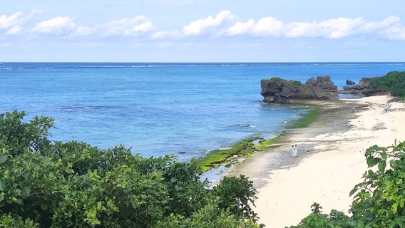 Eine Bucht mit blauem Wasser, darüber weiße Wolken, ein großer Felsen ist am hinteren Bildrand im Wasser, davor Sandstrand. © NDR Foto: Isa Hoffinger