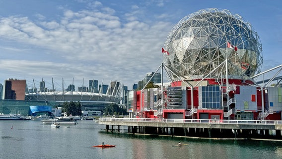 Ein kugelförmiges Gebäude direkt am Wasser, dahinter die Skyline von Vancouver mit Stadion © NDR Foto: Dennis  Burk