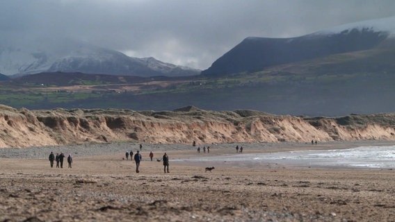 Menschen spazieren am wolkenverhagenen Strand von Wales © NDR Foto: Mathias Schuch