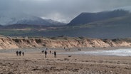 Menschen spazieren am wolkenverhagenen Strand von Wales © NDR Foto: Mathias Schuch