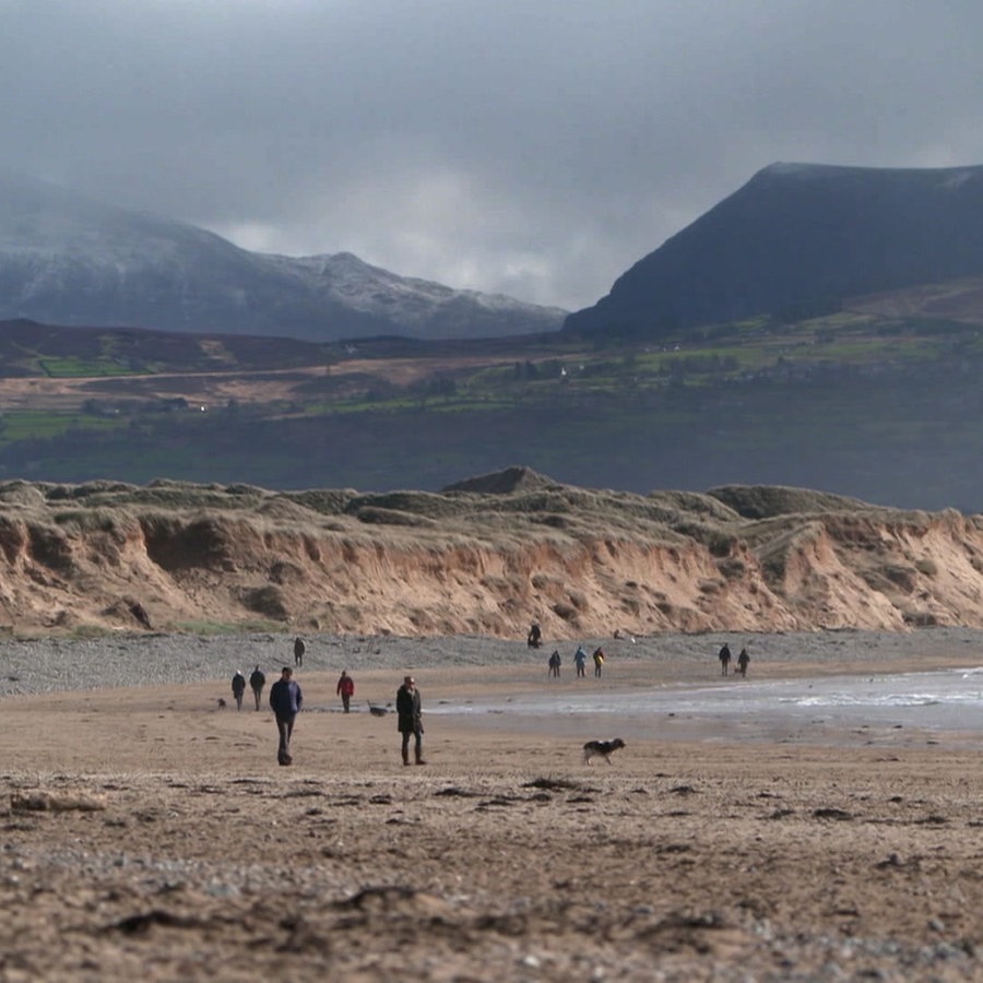 Menschen spazieren am wolkenverhagenen Strand von Wales © NDR Foto: Mathias Schuch